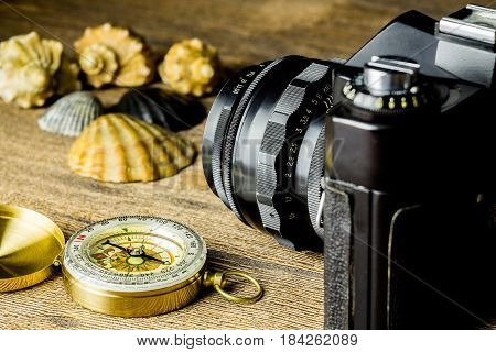 Old fotocamera with sea shells and compass on the brown wooden background