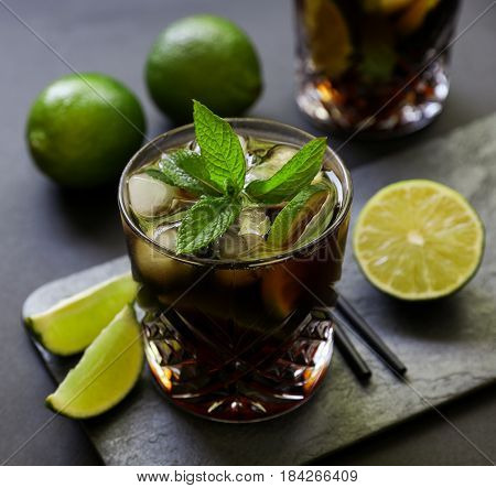 Cuba Libre or long island iced tea cocktail with strong drinks, cola, lime and ice in glasss, cold longdrink on dark background. Close-up.
