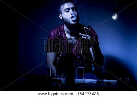 Young man with beard lost in the vices of alcoholism smoking and drug addiction