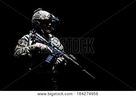 Bearded soldier in Combat Uniforms with weapon, plate carrier and combat helmet are on. Studio shot, dark background