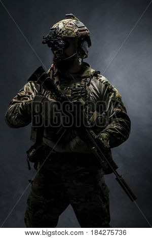 Bearded soldier in Combat Uniforms with weapon, plate carrier and combat helmet are on. Studio shot, dark background