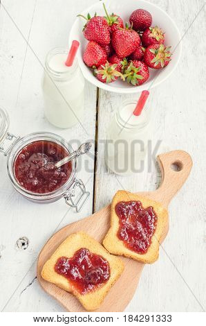 Toasts with strawberry jam and milk for breakfast on white rusric wooden background. Selective focus.
