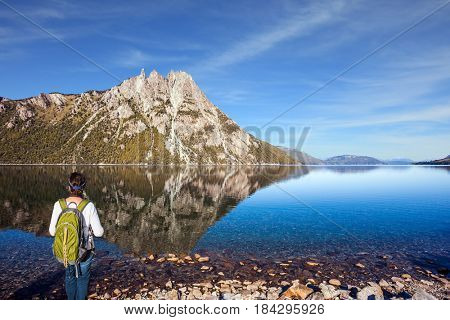 The elderly woman with green tourist backpack admires lake and mountain in Bariloche. The concept of exotic and extreme tourism. Picturesque summer in Argentina