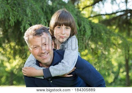Portrait of father with his son having fun in summer park. Piggyback. Family fun. Happy boy playing with dad summer nature outdoor