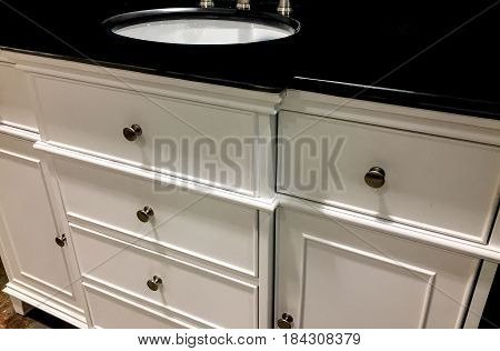 Interior design of a contemporary white bathroom cabinet and elegant dark granite counter top, porcelain sink and chrome knobs. Wooden cabinetry white bathroom style