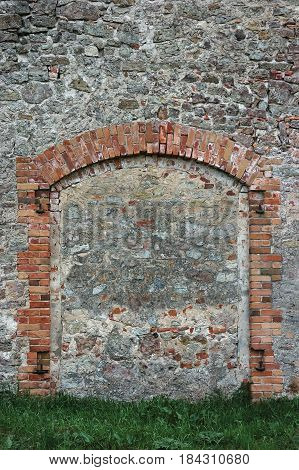 Barn gate door fake false faux arch, stone wall background frame closeup, vertical limestone copy space, green grass, plastered grunge red brick stonewall pattern, old aged weathered beige lime plaster texture, natural grungy textured reddish vintage roug