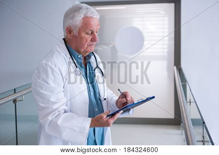 Doctor writing on clipboard in the passageway at hospital