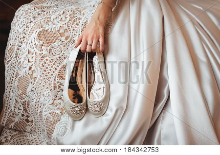 Bride holds the wedding shoes in her hands.