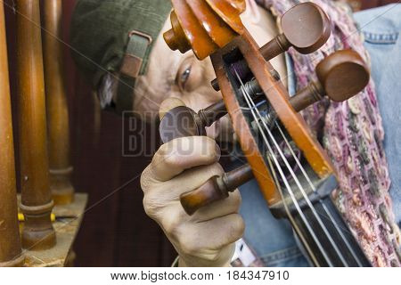A cellist tuning his cello with a serious look on his face focus in the foreground