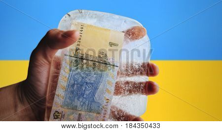 Ukrainian money in ice on a flag background. Devaluation, financial crisi.