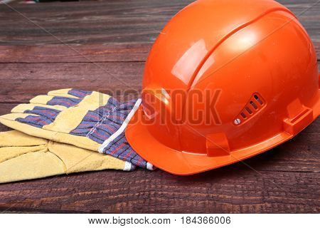 Orange hard hat and gloves for work on wood background