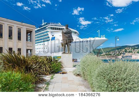 Trieste - August 2016, Friuli Venezia Giulia region, Italy: Harbor of Trieste, monument of Nazario Sauro, bronze statue of the famous sailor with cruise ship and blue sky on the background
