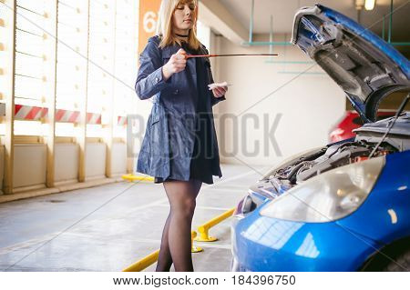 Woman Near Car's Hood. Young Blonde In Covered Parking Of Shopping Center, Stands Near Car With Rais