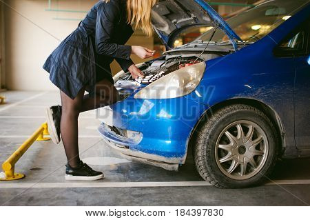 Woman Near Car's Hood. Young Blonde In Covered Parking Of Shopping Center, Stands Near Car With Engi