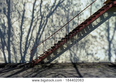 The stairs attached to the wall with no windows with the shadow of the trees