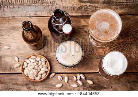 Beer in bottles and glasses on a wooden table. Beer and snacks pistachio nuts top view. Drink and snack for the football match or rest in pub