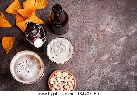 Beer in bottles and glasses on the concrete table. Beer and snacks are pistachio nuts chips and nachos top view. Copy space. Drink and snack for the football match or rest in pub