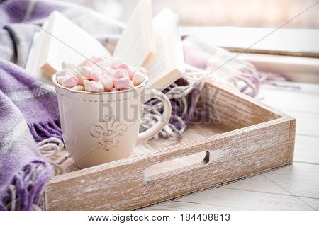 Coffee cup open book marshmallow and plaid on a window sill in winter. Concept warm and cozy home breakfast