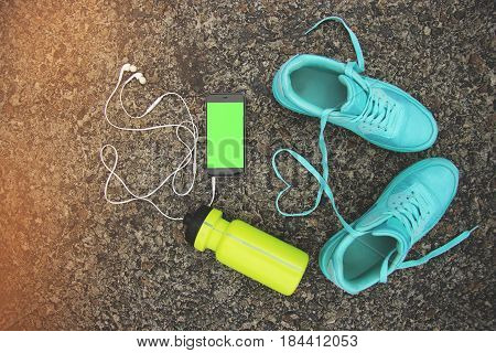Sports equipment and love concept. Portrait of blue sports shoes with shoelaces shaped in form of heart bottle of water and phone with green screen. Chromakey.
