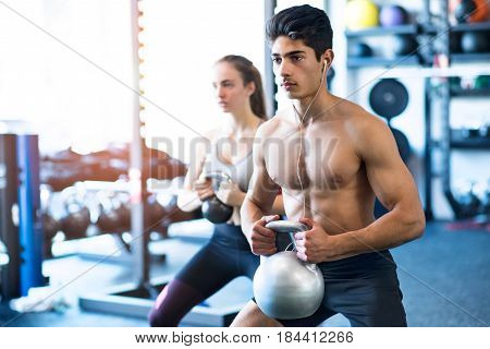 Beautiful young fit couple doing strength training, exercising with kettlebell in modern gym.