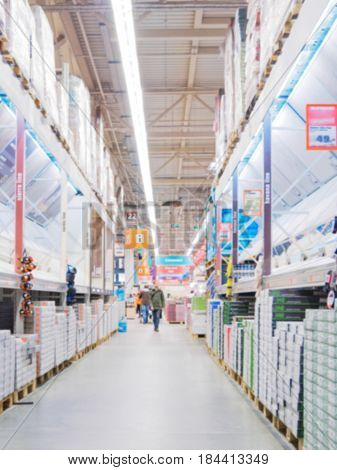 Abstract blurred hardware store aisle with finishing material shelves and unrecognizable customers as background. Vertical