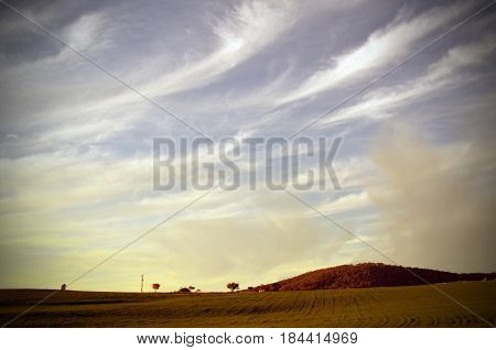 Wispy cirrus clouds over a sown field and hills at sunset in the NSW countryside, Australia