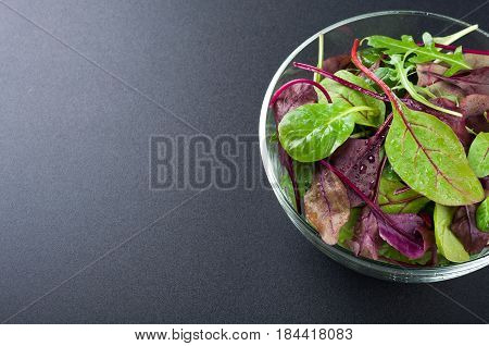 Fresh green salad with spinach arugula chard leaves lettuce. Mixed salad leaves on dark background. Healthy food healthy lifestyle and diet concept. Top view. Copy space