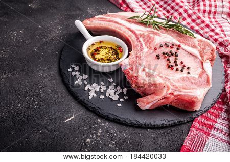 Raw meat with herbs oil and spices on dark background. Raw pork steak. Ingredients for cooking meat