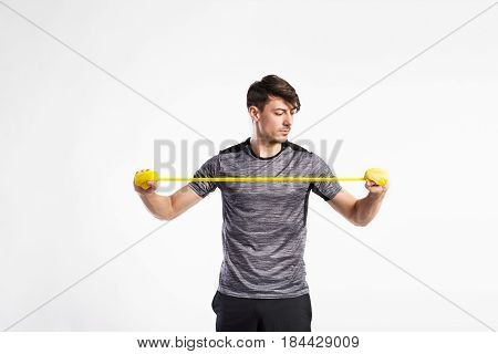 Handsome fitness man in gray t-shirt working out with rubber band. Studio shot on gray background.
