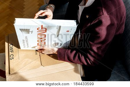 PARIS FRANCE - APRIL 24 2017: Woman unboxing new book Living Doing Working & Enjoying: Red Dot Design Yearbook shows current award-winning products