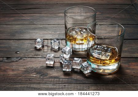 Two glasses of whiskey with ice cubes served on wooden planks. Vintage countertop and a glass of hard liquor.