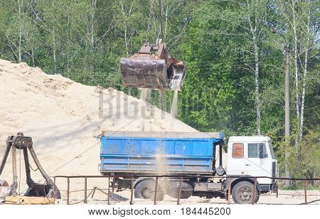 wheel loader excavator machine loading dumper truck at sand quarry.
