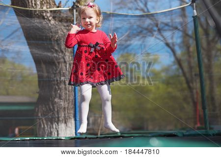 Little Girl In A Red Dress Jumping On A Trampoline In The Park