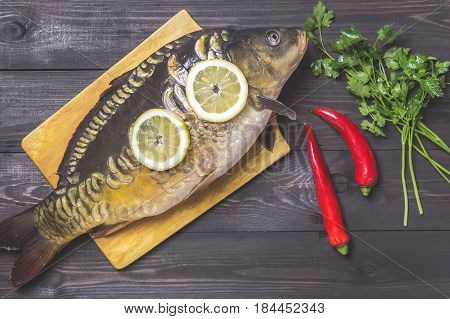 Mirror carp river fish with lemon herbs and pepper on dark wooden table.