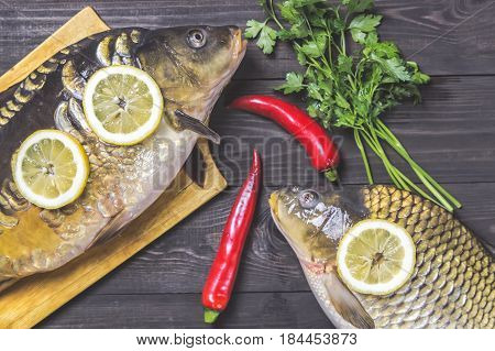 Mirror carps river fish with lemon herbs and pepper on dark wooden table.