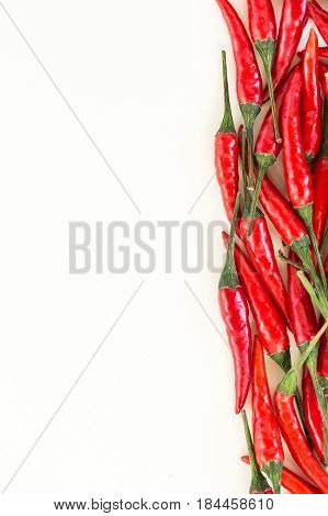 spicy food-making, popular spices concept - close-up on a pure and delicious fresh red hot peppers with green tails are grouped vertically on a white background , top view, flat lay, vertical