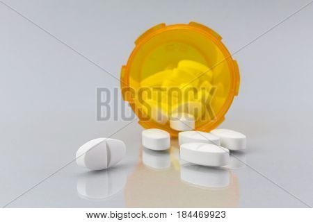Pills spilling from an open bottle on white backgroubd