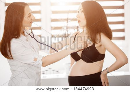 Female Medicine Doctor Holding Stethoscope To Pregnant Woman Standing For Encouragement, Empathy, Ch