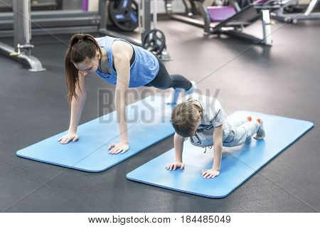 mother and son in sport shirts are doing plank in gym.