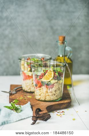 Healthy vegan energy boosting salad with quionoa, avocado, dried tomatoes, basil, olive oil, mint in glass jars, marble background, selective focus, copy space. Clean eating, vegan, detox food concept