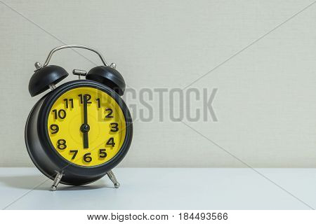 Closeup yellow and black alarm clock for decorate in 6 o'clock on white wood desk and cream wallpaper textured background with copy space