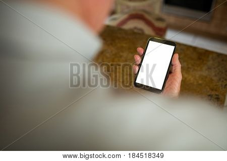 Senior man holding mobile phone in the ktchen at home