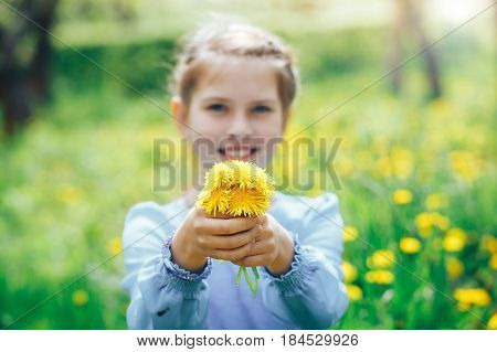 beautiful blue-eyed and blond girl in a meadow holding a dandelion in the hands