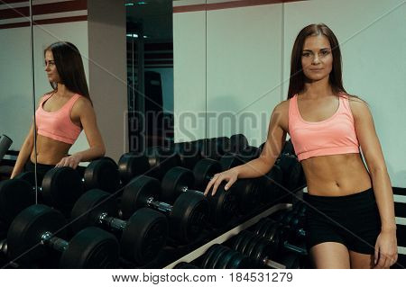Beautiful girl standing near mirror and a dumbbell in the gym.