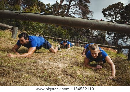 Fit people crawling under the net during obstacle course in bootcamp