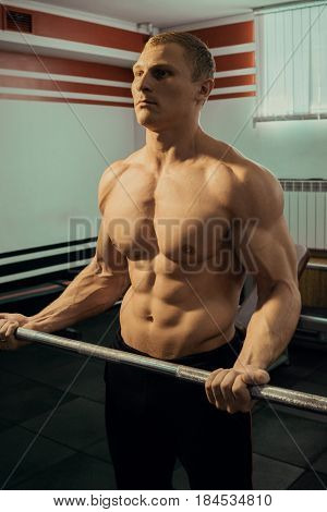 young muscular man with naked torso raises the bar in the gym. Fitness