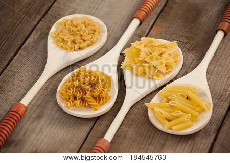 Spoons filled with varieties of pasta on wooden background