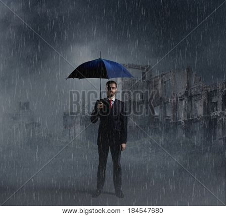Businessman with umbrella standing over apocalyptic background. Crisis, default, setback concept.