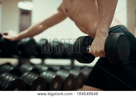Closeup of a muscular young man lifting weights in gym.