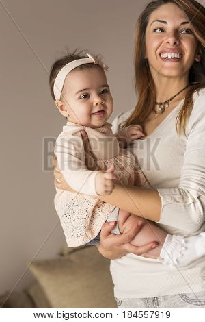 Young mother holding and hugging her baby girl while both enjoying their time together. Focus on the baby